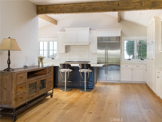 kitchen featuring vaulted ceiling with beams, stainless steel appliances, white cabinetry, light countertops, and a kitchen bar