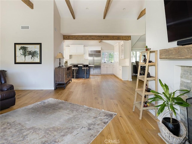 living room featuring visible vents, beamed ceiling, light wood-style flooring, and baseboards