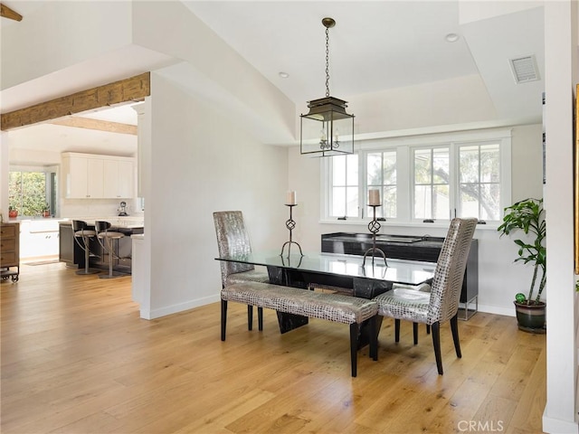 dining area featuring light wood-style floors, a tray ceiling, visible vents, and baseboards