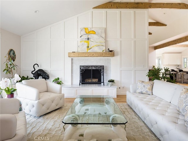 living room featuring light wood-type flooring, a decorative wall, lofted ceiling with beams, and a premium fireplace