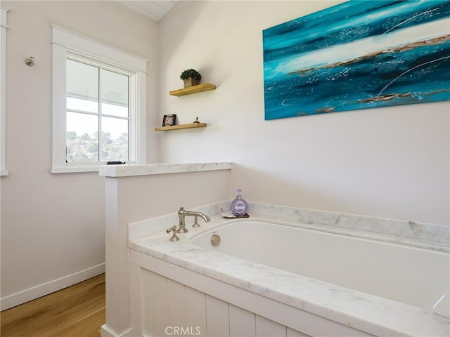 bathroom with baseboards, a bath, and wood finished floors