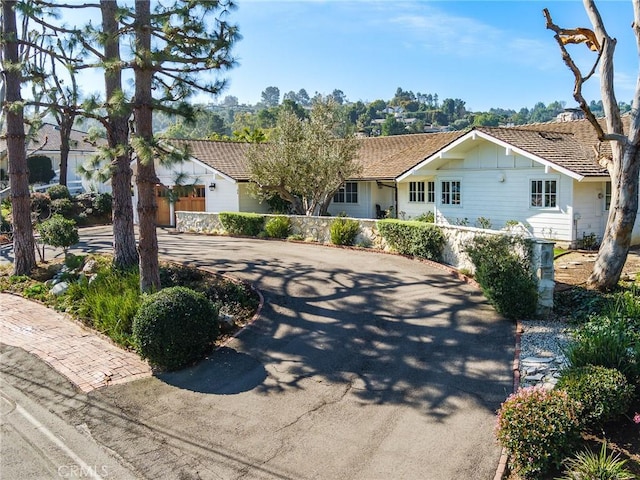 ranch-style home with a tiled roof, board and batten siding, curved driveway, and fence