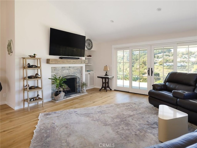 living area with french doors, a fireplace, light wood finished floors, vaulted ceiling, and baseboards