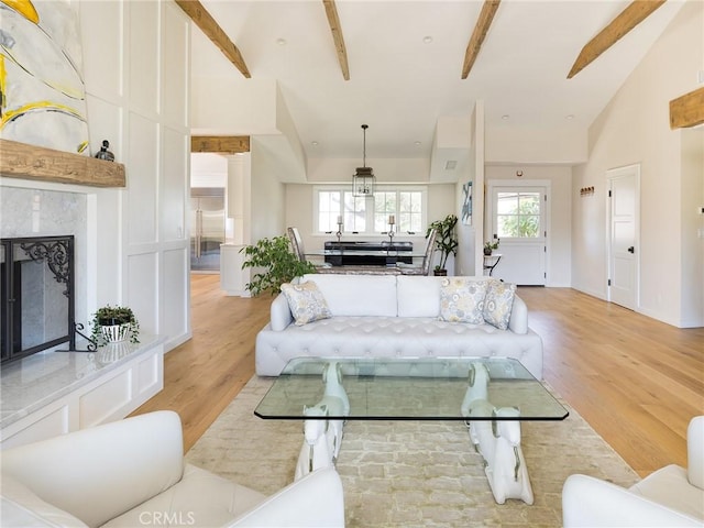 living area with light wood finished floors, a fireplace, and beamed ceiling