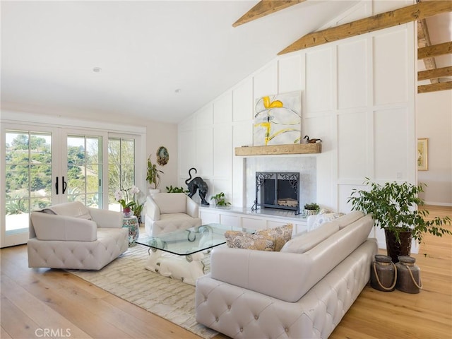 living room with a fireplace with raised hearth, high vaulted ceiling, a decorative wall, light wood-style floors, and beam ceiling