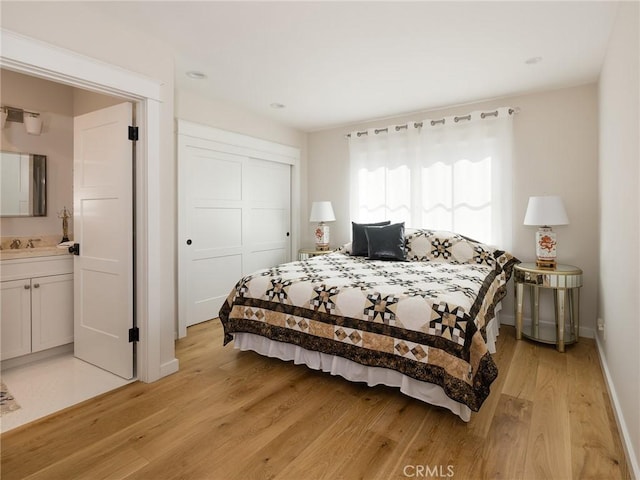 bedroom with a closet, baseboards, ensuite bath, light wood-style floors, and a sink