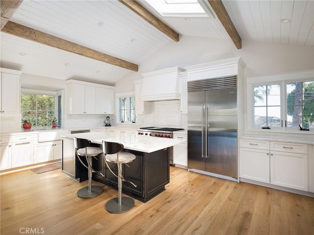 kitchen featuring premium range hood, a breakfast bar, a kitchen island, white cabinets, and high end appliances