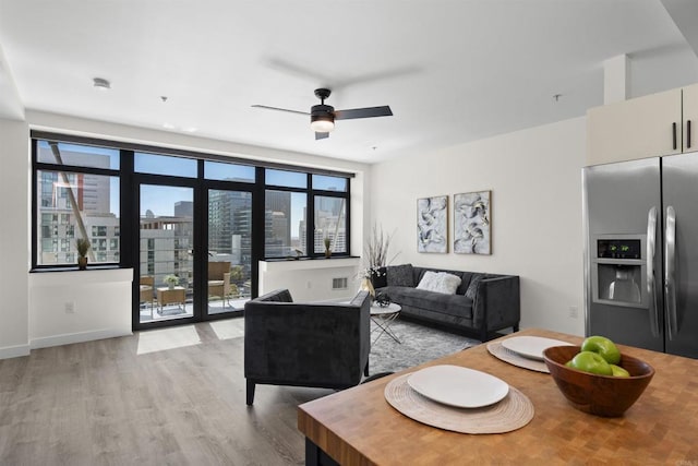 living area featuring baseboards, light wood-type flooring, a ceiling fan, and a city view