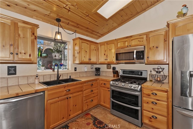 kitchen with stainless steel appliances, decorative light fixtures, a sink, and tile countertops