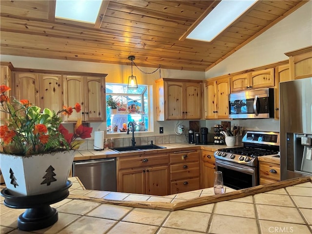 kitchen with pendant lighting, tile counters, appliances with stainless steel finishes, lofted ceiling with skylight, and a sink