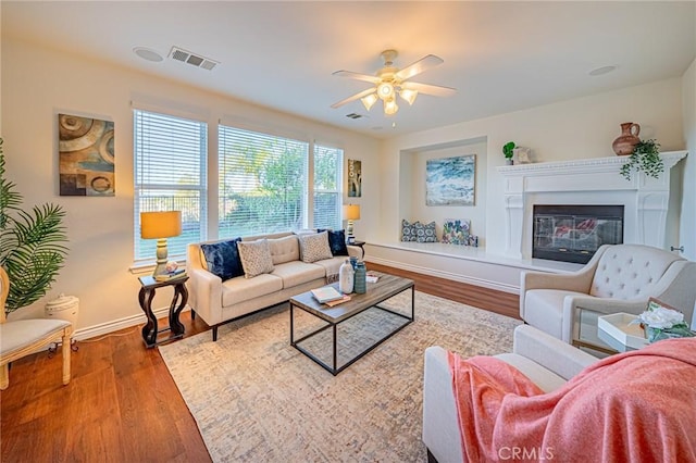 living area featuring baseboards, visible vents, wood finished floors, and a glass covered fireplace