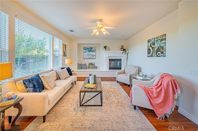 living area with baseboards, visible vents, a glass covered fireplace, ceiling fan, and wood finished floors