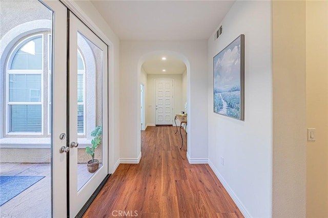 corridor featuring arched walkways, wood finished floors, visible vents, and baseboards