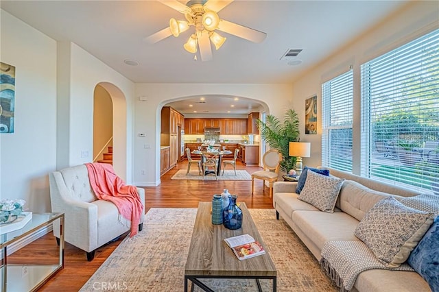 living room with arched walkways, visible vents, stairway, a ceiling fan, and wood finished floors