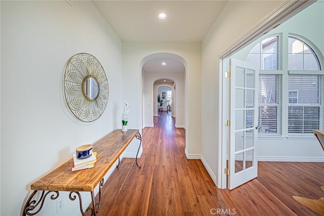 corridor featuring arched walkways, recessed lighting, wood finished floors, and baseboards