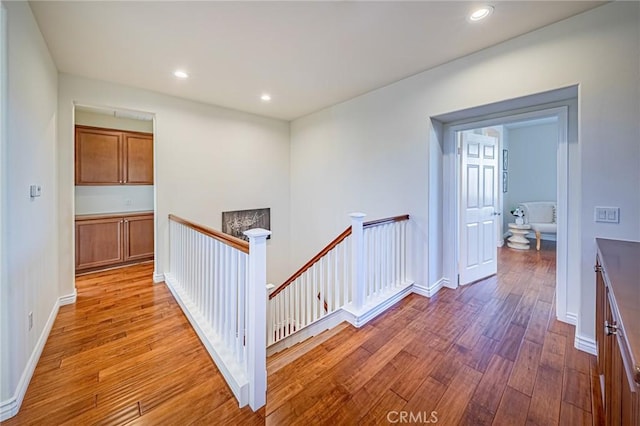 corridor with recessed lighting, baseboards, wood finished floors, and an upstairs landing