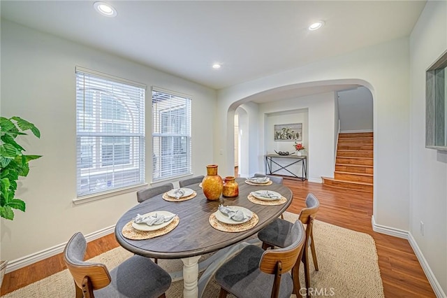 dining room with arched walkways, recessed lighting, wood finished floors, baseboards, and stairs