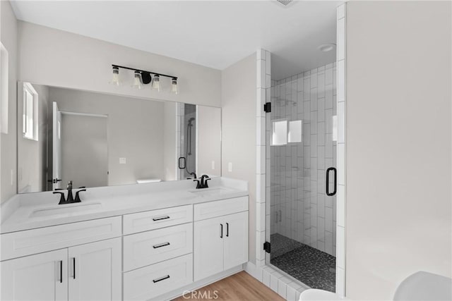 full bath featuring double vanity, a stall shower, a sink, and wood finished floors