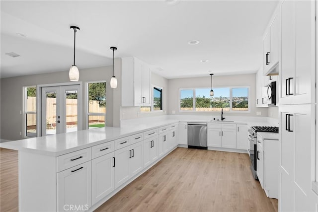 kitchen with a peninsula, a sink, white cabinets, light countertops, and appliances with stainless steel finishes