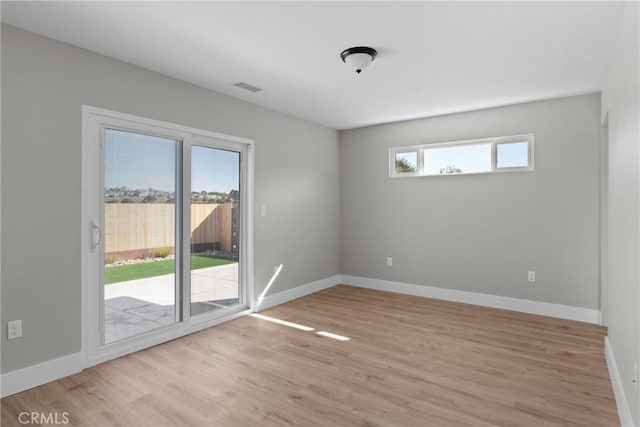 empty room with light wood finished floors, visible vents, and baseboards