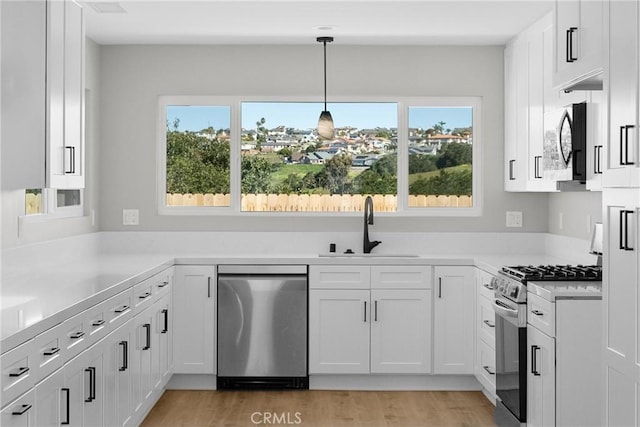 kitchen featuring appliances with stainless steel finishes, white cabinets, light countertops, and pendant lighting