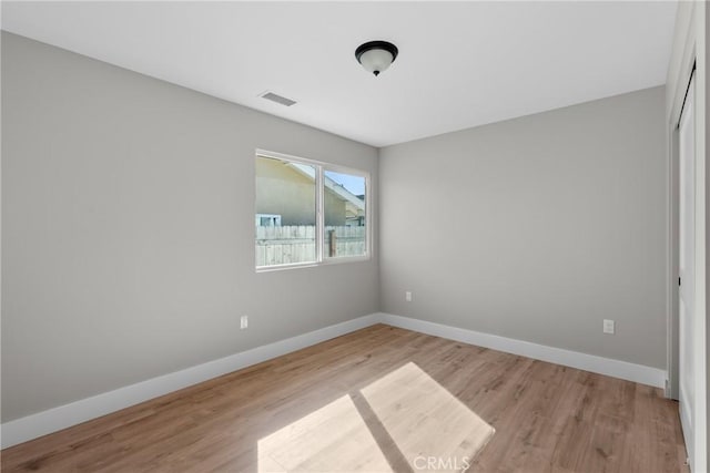 empty room with light wood finished floors, visible vents, and baseboards