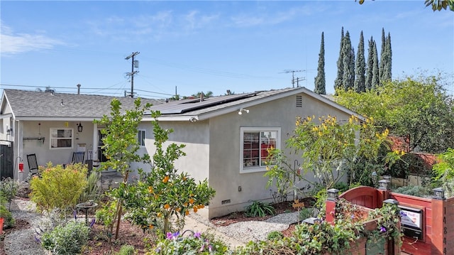 rear view of house featuring roof mounted solar panels, roof with shingles, and stucco siding