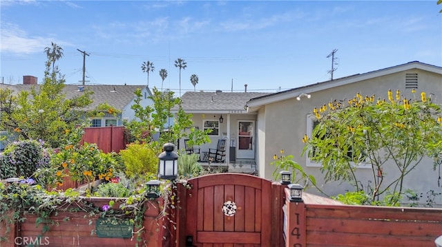 view of front facade with a fenced front yard, a gate, roof with shingles, and stucco siding