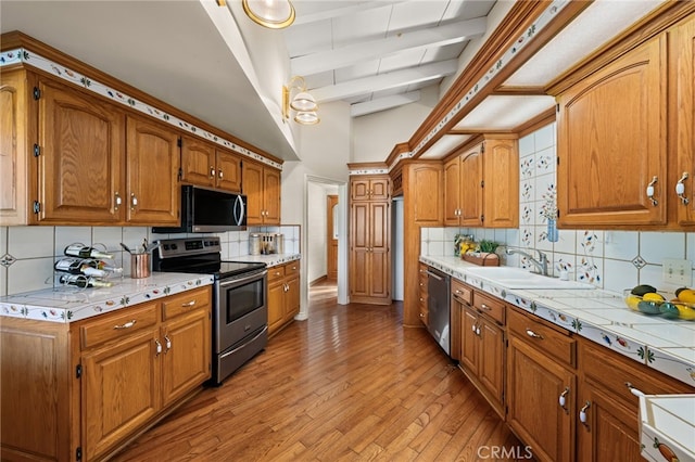 kitchen with beam ceiling, tasteful backsplash, light countertops, light wood-style flooring, and appliances with stainless steel finishes