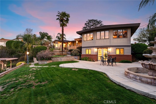 back of property at dusk featuring a patio area, a lawn, and brick siding