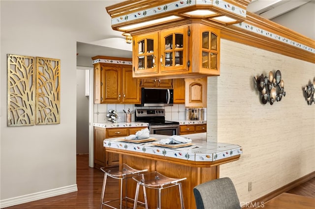 kitchen with decorative backsplash, brown cabinets, dark wood-style flooring, stainless steel appliances, and light countertops