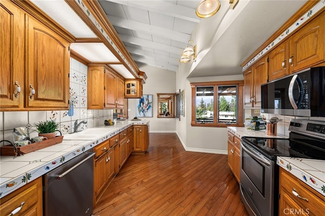 kitchen featuring stainless steel appliances, tile counters, lofted ceiling with beams, decorative backsplash, and a sink