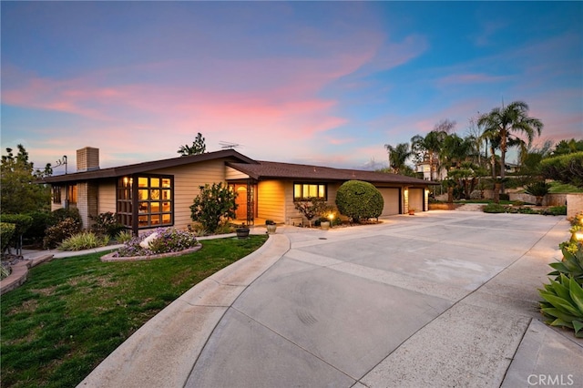 mid-century inspired home with an attached garage, a chimney, a lawn, and concrete driveway