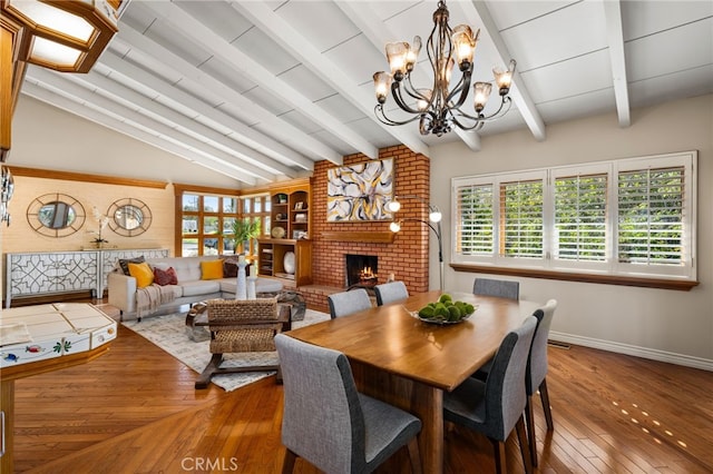 dining area featuring baseboards, lofted ceiling with beams, hardwood / wood-style floors, an inviting chandelier, and a fireplace