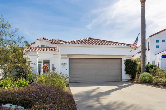 mediterranean / spanish-style house featuring a garage, concrete driveway, a tiled roof, and stucco siding