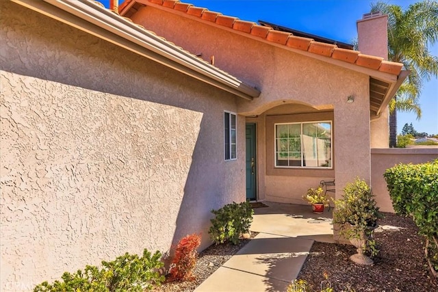 property entrance featuring a patio area, fence, a tile roof, and stucco siding