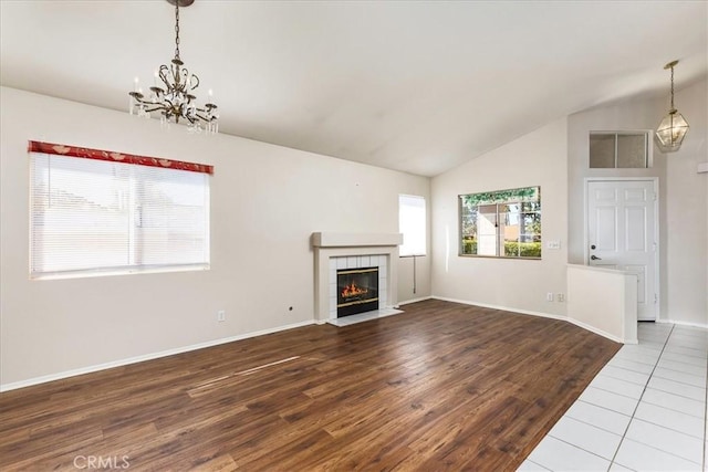 unfurnished living room with a chandelier, a fireplace, vaulted ceiling, and wood finished floors