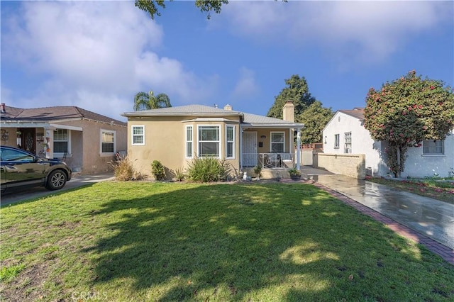 view of front of home featuring a front yard, a chimney, covered porch, and stucco siding