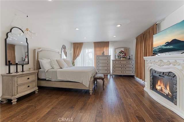 bedroom with dark wood-style floors, a glass covered fireplace, and recessed lighting