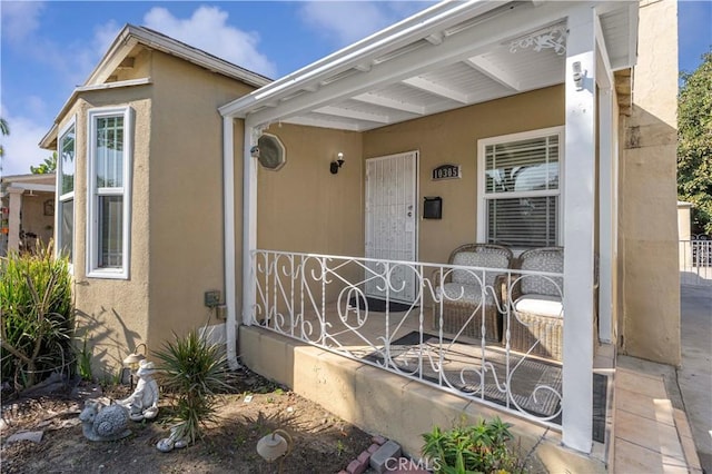 property entrance with covered porch, stucco siding, and fence