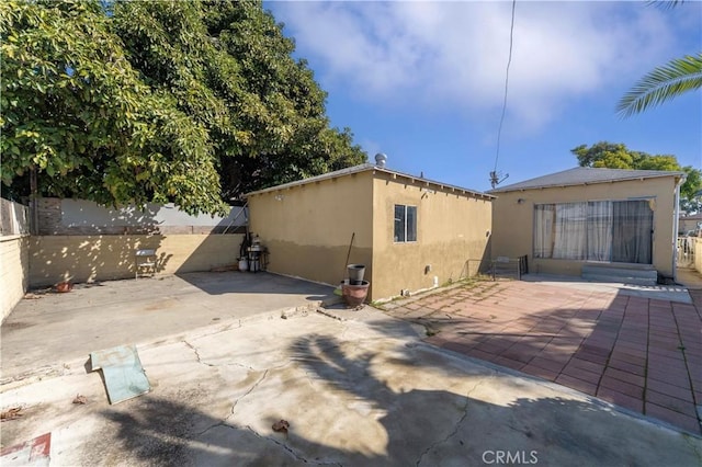 exterior space featuring a patio, fence, an outbuilding, and stucco siding