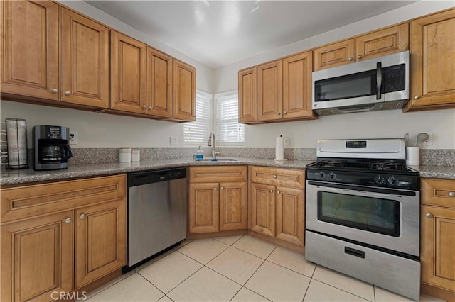 kitchen with a sink, appliances with stainless steel finishes, light tile patterned flooring, and brown cabinetry