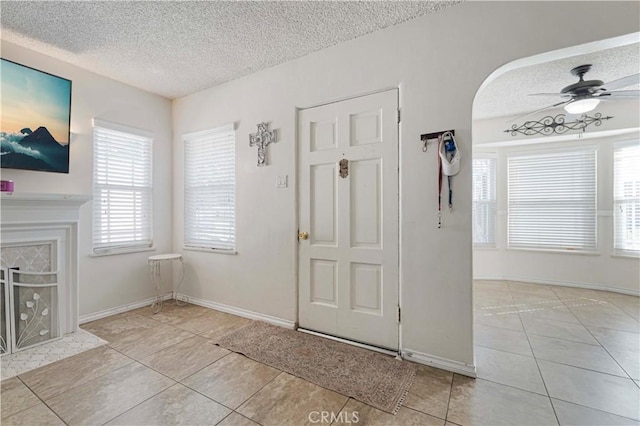 tiled entrance foyer featuring baseboards, a tile fireplace, a textured ceiling, and a ceiling fan