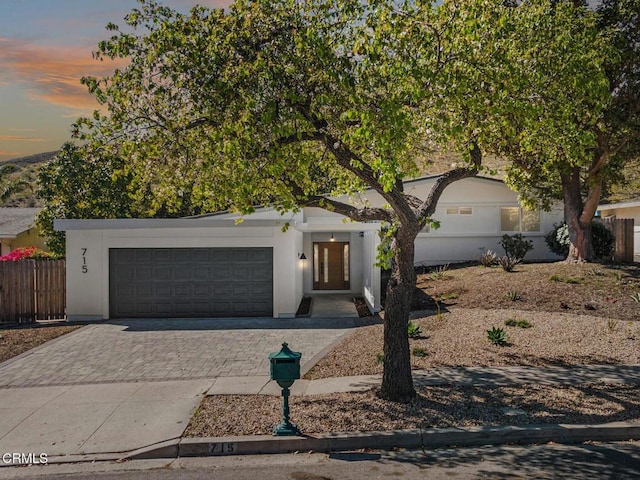 view of front of house with a garage, decorative driveway, fence, and stucco siding