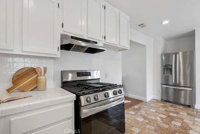 kitchen featuring stainless steel appliances, tile counters, white cabinetry, under cabinet range hood, and baseboards