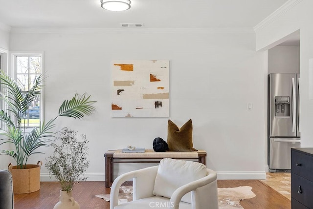 living area featuring baseboards, wood finished floors, visible vents, and crown molding