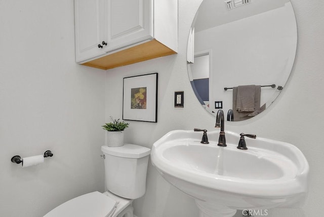 half bath with toilet, visible vents, and a sink