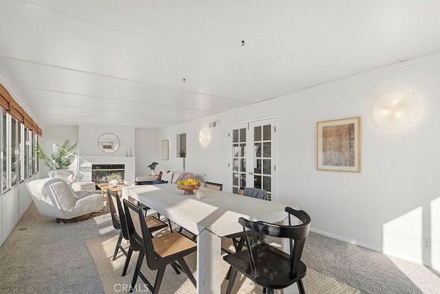 dining room featuring light carpet, a brick fireplace, and french doors