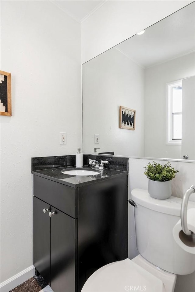 half bathroom featuring ornamental molding, baseboards, vanity, and toilet