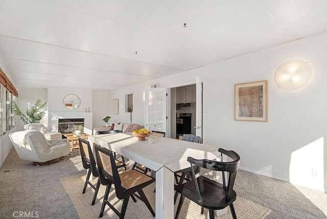 dining space featuring a large fireplace and light colored carpet